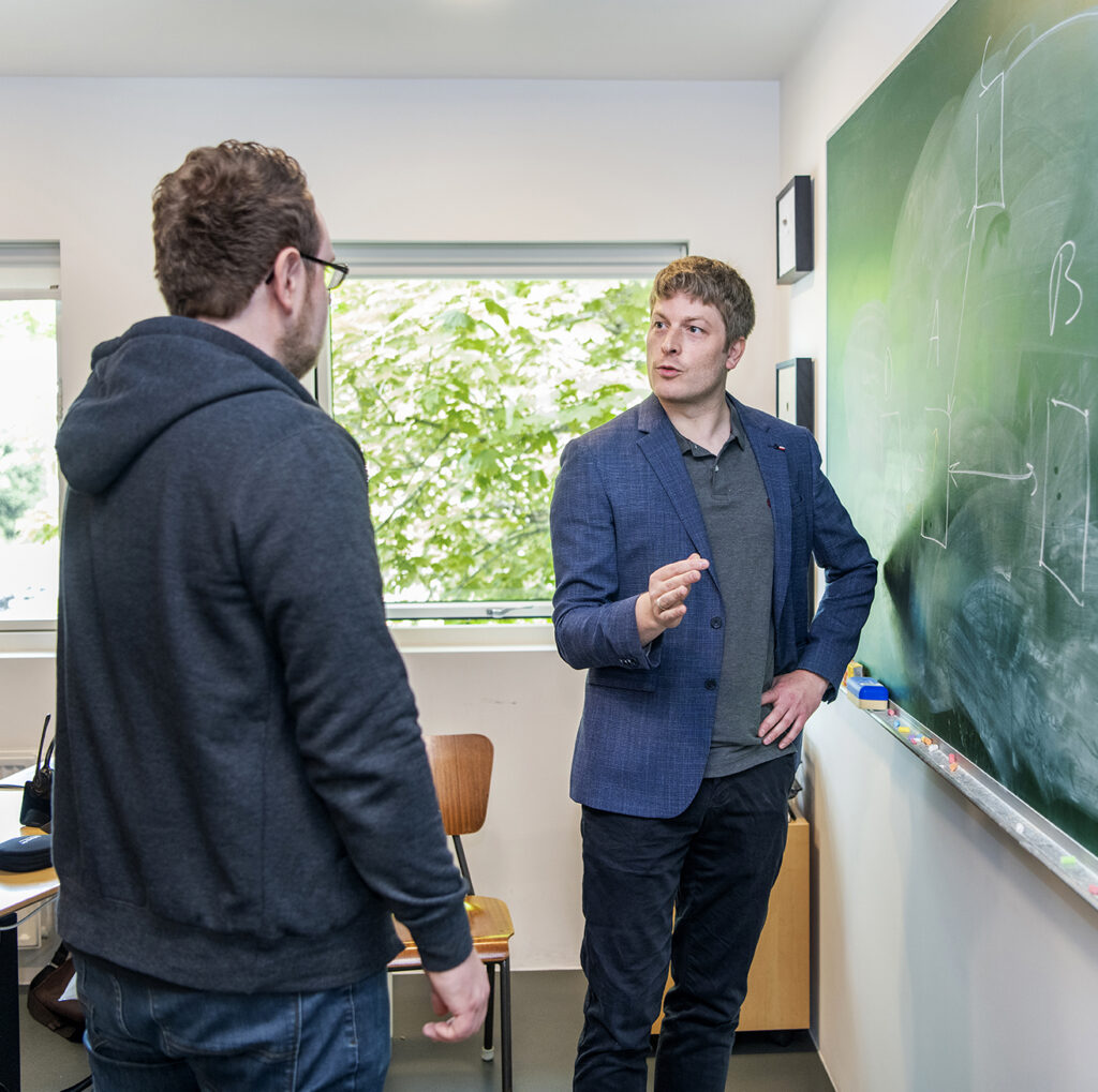 Kollegaer fra SkoleIT står og taler sammen i et klasselokale med tavle